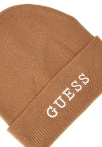Beanie marrone a maglia con risvolto e logo "GUESS" bianco ricamato sul davanti. Texture morbida e design aderente.