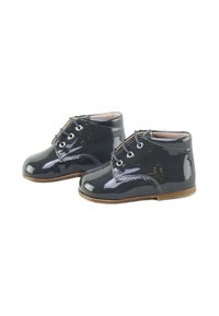 Zapatos de charol negro hasta el tobillo con cordones, forma de punta redonda, suela de goma marrón y un sutil detalle de costura en los laterales.