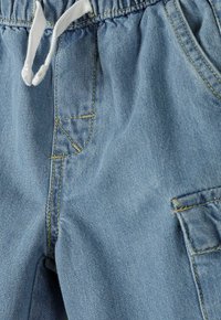 Gai zils džinsu joggers ar elastīgu jostu, baltu auklu, divām sānu kabatām un kontrastējošiem dzelteniem izšuvumiem.