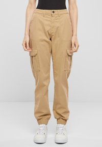 Beige cargo kalhoty s elastickými manžetami, dvěma bočními kapsami a zapínáním na knoflík. Vyrobeny z odolné bavlněné tkaniny.
