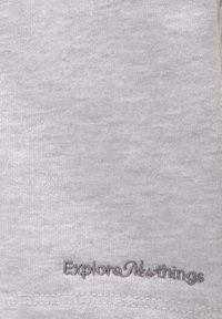 Lyst gråt stof med små broderede mørke bogstaver nær kanten, der står "Udforsk nye ting" i kursiv.