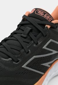Black athletic shoe featuring a textured upper, grey accents, and orange details. Includes laces, a cushioned tongue, and a lightweight white sole.