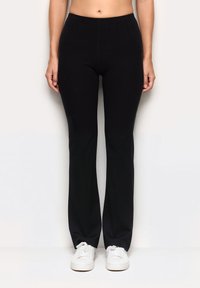 Czarne, elastyczne spodnie z dopasowaną talią i rozkloszowanymi nogawkami, wykonane z miękkiego materiału. W parze z białymi trampkami, tworząc swobodny look.