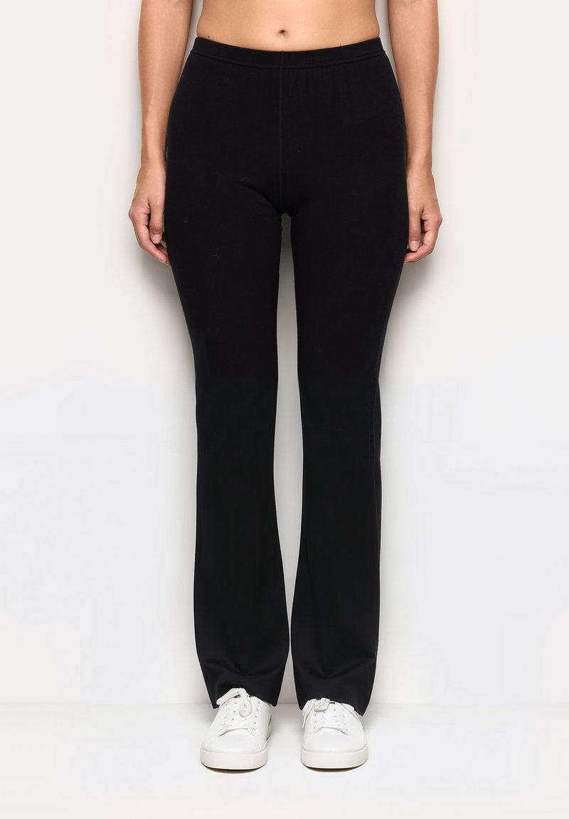 Czarne, elastyczne spodnie z dopasowaną talią i rozkloszowanymi nogawkami, wykonane z miękkiego materiału. W parze z białymi trampkami, tworząc swobodny look.