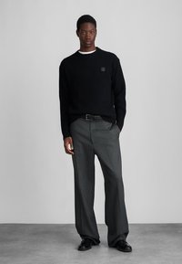 Fekete bordázott pulóver kicsi logóval, szürke bővebb nadrággal párosítva. Az öltözéket fekete öv és cipő egészíti ki.