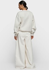 Sweat-shirt gris clair surdimensionné avec épaules tombantes, associé à un pantalon blanc à jambes larges, présentant une texture douce et une coupe décontractée.