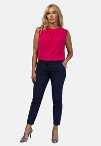 Fuksjowy top bez rękawów z plisami, w połączeniu z granatowymi spodniami w wzory i obcasami w wężowy wzór. Prosty design, żywe kolory i fakturowane akcenty.