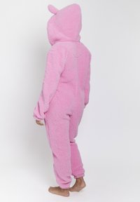 Tuta in pile rosa con cappuccio dotato di piccole orecchie, vestibilità comoda, polsini elasticizzati e una superficie morbida e strutturata.