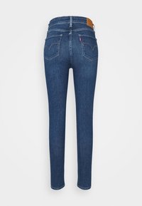 Jean skinny en denim bleu foncé, avec une taille mi-haute, un design à cinq poches, et un patch en cuir sur la ceinture arrière.