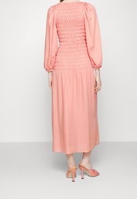 Pitkähihaisen, puffimaiseen mekkoon, joka on pehmeän vaaleanpunainen, on smokkikaulus ja virtaava hameosa. Yhdistetty samansävyisiin korkokenkiin. Tasainen tekstuuri kauttaaltaan.