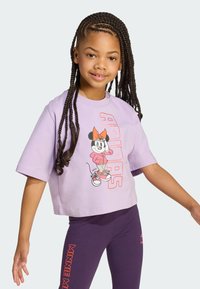 Lilla lühikeste varrukatega cropped t-särk, millel on Minnie Mouse graafika ja tekst "ADIDAS". Sobitatud lilla retuusidega, millel on tekst "MINNIE MAE."