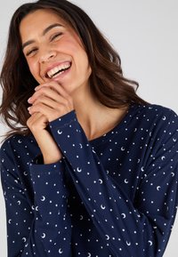 Marineblauwe longsleeve top van zacht materiaal, met een patroon van kleine witte sterren en halfmanen. Ronde halslijn en strakke boorden.