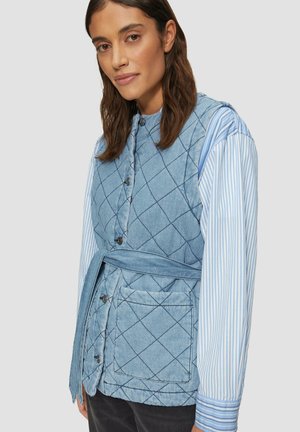 Gepolsterte Jeansweste in Hellblau mit einem Gürtel, mit einer knöpften Front und einer aufgesetzten Tasche. Darunter ein blau-weiß gestreiftes Langarmhemd.