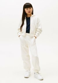 Hvid cropped hoodie med en frontlynlås, en navy skjorte under, og matchende hvide sweatpants. Har elastiske manchetter og snor i taljen.