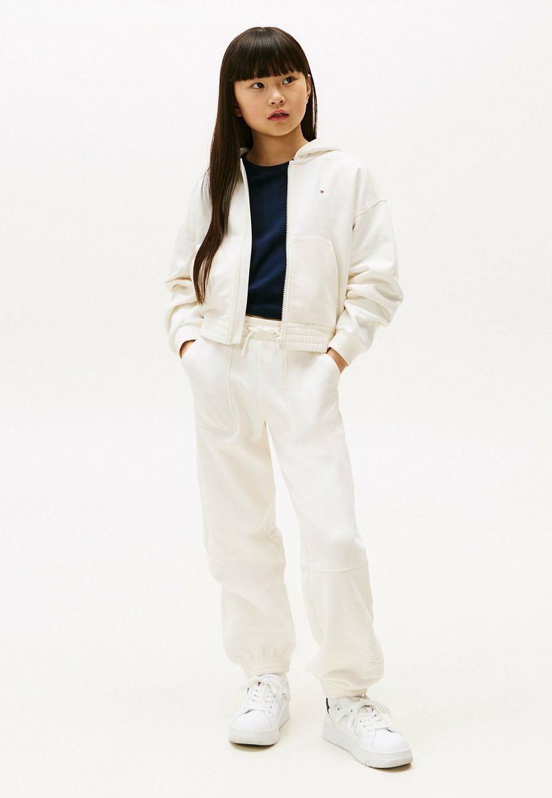Hvid cropped hoodie med en frontlynlås, en navy skjorte under, og matchende hvide sweatpants. Har elastiske manchetter og snor i taljen.