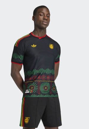 Uomo che indossa una maglia sportiva nera e pantaloncini con accenti verdi, rossi e gialli, che presentano l'emblema della Giamaica e motivi ispirati al reggae.