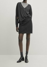 Haut à manches longues gris foncé avec col en V superposé sur une chemise gris clair, associé à une jupe ajustée assortie et des chaussures noires à lacets.