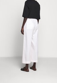 Svart oversized T-shirt och vita vida byxor, tillverkade av bomull med en slät yta; byxorna har bakfickor och synliga sömnadsdetaljer.