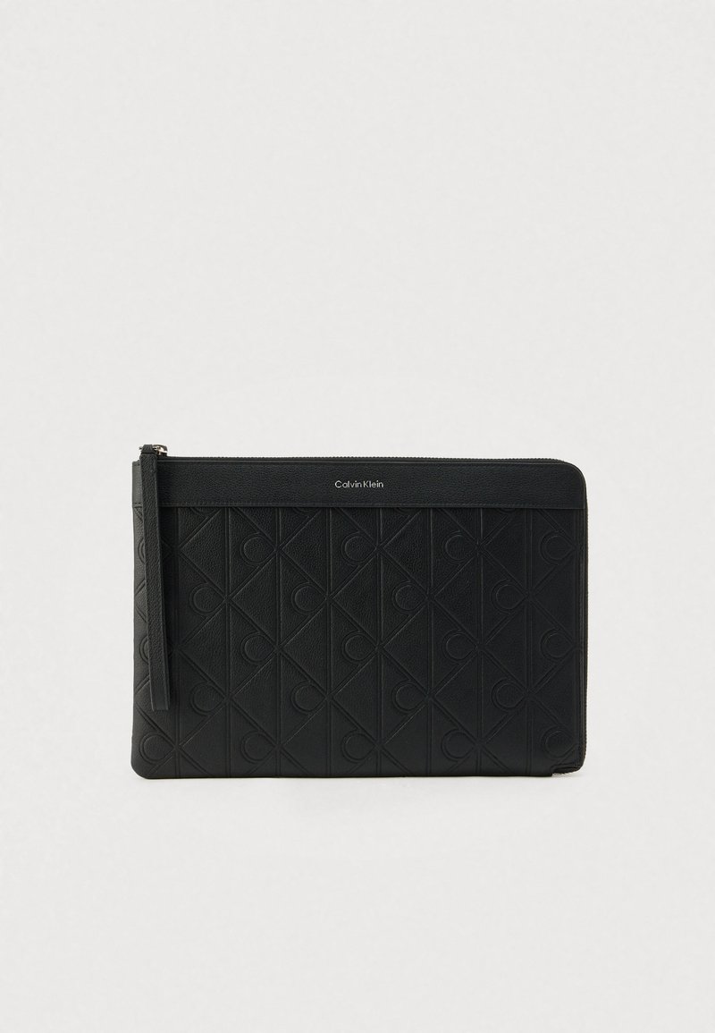 Pochette en cuir noir avec un motif géométrique texturé, dotée d'une fermeture éclair supérieure et d'une bande de marque affichant "Calvin Klein".