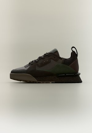 Baskets vert foncé et noir avec matériaux mixtes, semelle épaisse et languette au talon, vues de côté sur fond neutre.