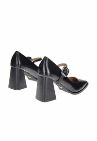 Scarpe con tacco quadrato in pelle nera con punta affilata e cinturino alla caviglia con fibbia rettangolare. Texture liscia e lucente.