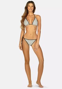 Czarny i biały bikini w kropki z trójkątnym stanikiem i cienkimi ramiączkami, z czarnymi wykończeniami i małym metalowym akcentem na środku.