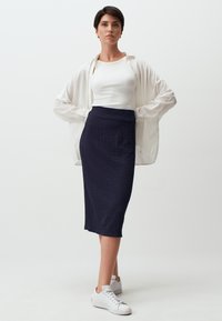 Gonna a matita blu navy con tessuto testurizzato abbinata a un top a canotta bianco con costine e una camicia trasparente a maniche lunghe, completata da sneakers bianche.