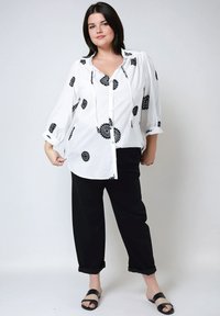 Witte blouse met zwarte bloemenborduursel, driekwart mouwen, knopen aan de voorkant. Zwarte cropped broek en zwarte slide sandalen maken de outfit compleet.