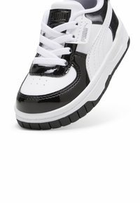 Czarno-białe trampki z lakierowanej skóry i gładkiego materiału tekstylnego, z zaokrąglonym noskiem, gumową podeszwą i wyraźnym logo na języku.