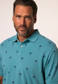 Turkusowa koszulka polo wykonana z mieszanki bawełny, z powtarzającym się nadrukiem palm w ciemnym niebieskim kolorze. Krótkie rękawy i klasyczny krój kołnierzyka.