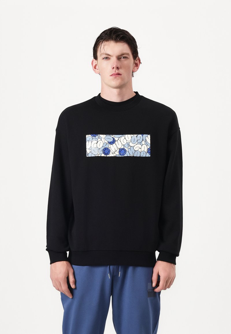 Sudadera negra con cuello redondo, que presenta un gráfico rectangular en azul sobre blanco, que representa texto estilizado y formas abstractas.