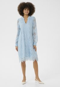 Svetle modré krajkové šaty s výstřihem do V, dlouhými průhlednými rukávy a složitými vzory; volánkový lem přidává jemný detail.