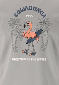 Grå stof t-shirt med en cartoon flamingo iført solbriller og skateboard, omgivet af palmetræer. Teksten lyder "COWABUNGA DUDE" og "FRI TIL AT KØRE PÅ BØLGERNE."