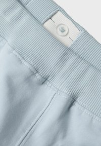 Shorts décontractés bleu clair avec une taille côtelée, une étiquette en tissu blanche et une fermeture à un bouton. Texture lisse et coutures propres.