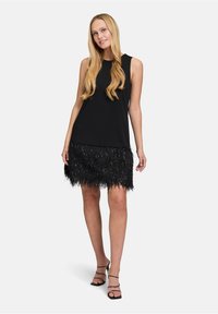 Czarny bezrękawnik o luźnym kroju, zestawiony z frędzlowaną czarną spódnicą z błyszczącymi akcentami na dolnej krawędzi. Stylizację dopełniają sandały.