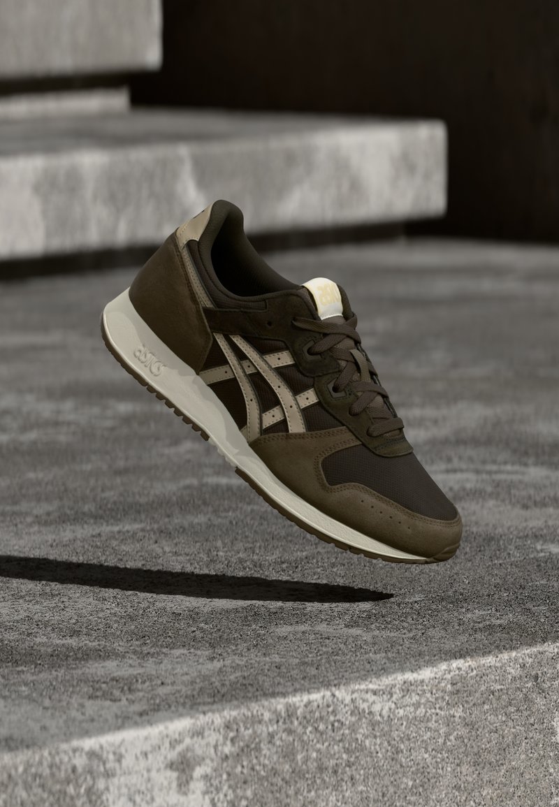 Buty sportowe z ciemnooliwkowym cholewką, wykonane z siateczki i zamszu, z kremowymi akcentami oraz teksturowaną gumową podeszwą. Sznurówki w kolorze brązowym.