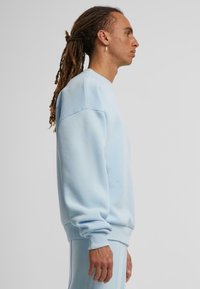 Hellblaues Sweatshirt mit lockerer Passform, gerippten Bündchen und Rundhalsausschnitt, aus weichem Material mit glatter Textur.