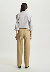 Chemise légère à rayures blanche et pastel, associée à un pantalon beige taille haute. Les deux vêtements ont une coupe décontractée et un minimum de détails.
