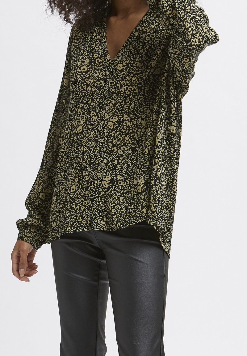 Blouse à motif noir et vert avec un décolleté en V, des manches ballon longues et une coupe décontractée, assortie à un pantalon en cuir synthétique noir.