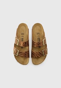 Sandales en cuir marron avec deux sangles réglables, présentant un motif texturé et des accessoires couleur or. Semelle en liège, design léger.