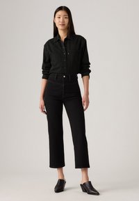 Camicetta di jeans nera con due tasche sul petto, abbinata a jeans neri a vita alta con gamba dritta, e mule neri con tacco.