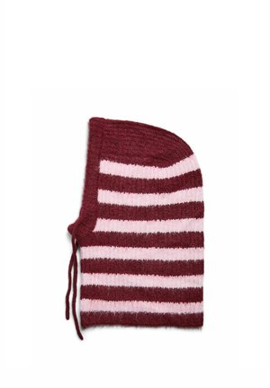 Femme portant une doudoune brillante couleur bordeaux et une capuche en laine rayée aux couleurs bordeaux et rose, mains dans les poches, expression neutre.