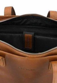 Braune Ledertasche mit einem Reißverschluss, schwarzem Stoffinneren und einem mit "LAPTOP" gekennzeichneten Etikett im Inneren. Glatte Textur und minimalistisches Design.