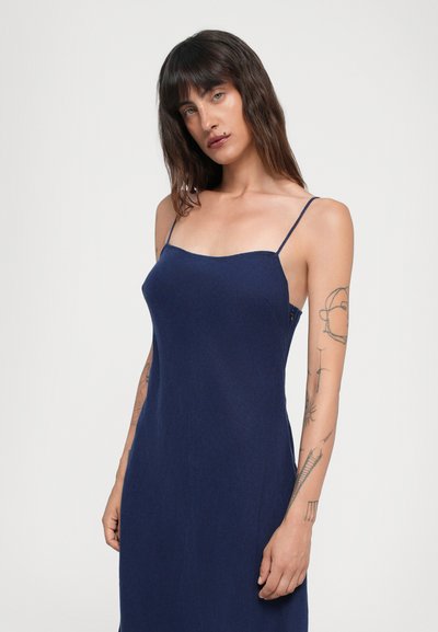 Vestido de marina sin mangas con tirantes finos, silueta ajustada, textura suave y un brillo sutil. Presenta un escote cuadrado y aberturas laterales.