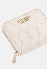 Portafoglio in pelle trapuntata crema con logo GUESS dorato, chiusura con zip e motivo a rombi cucito.