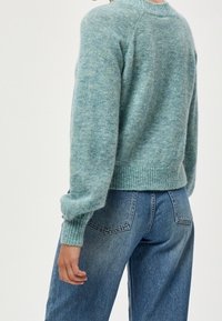 Maglione lavorato a maglia blu chiaro con orlo e polsini a coste, abbinato a jeans in denim blu a vita alta con tasche posteriori e una leggera scoloritura.
