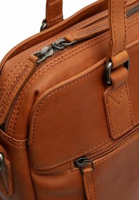 Tan leren tas met een gladde textuur, voorzien van dubbele ritsen en versterkte stiksels. Inclusief een buitenzak en stevige handvatten.