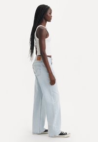 Jean large bleu clair en denim, avec une taille haute, des poches latérales et une étiquette en cuir au dos. Assorti avec un débardeur blanc.