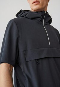 Sudadera negra con mangas cortas, con cierre de cremallera y un bolsillo frontal con solapa, fabricada en tejido suave.