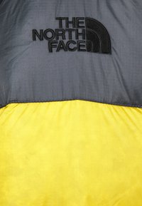 Kurtka ocieplana z czarną górną częścią w delikatny wzór kratki oraz żywiołową żółtą dolną częścią. Wyraźnie widoczne logo The North Face.